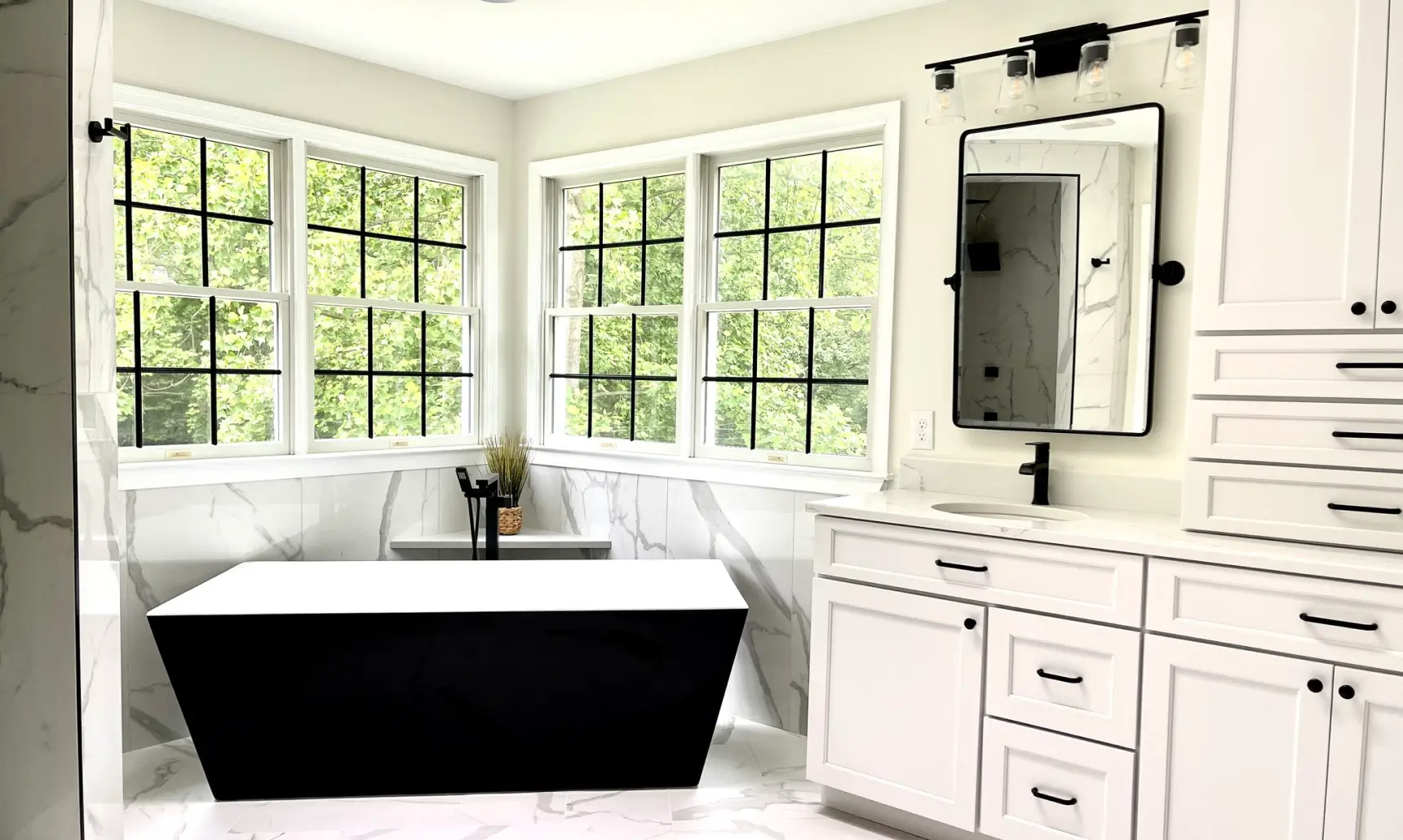Modern bathroom with a black freestanding tub, large windows, white cabinets, and a marble floor.