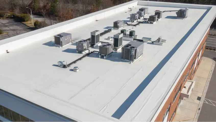 Aerial view of a large white rooftop with several HVAC units and exhaust fans.