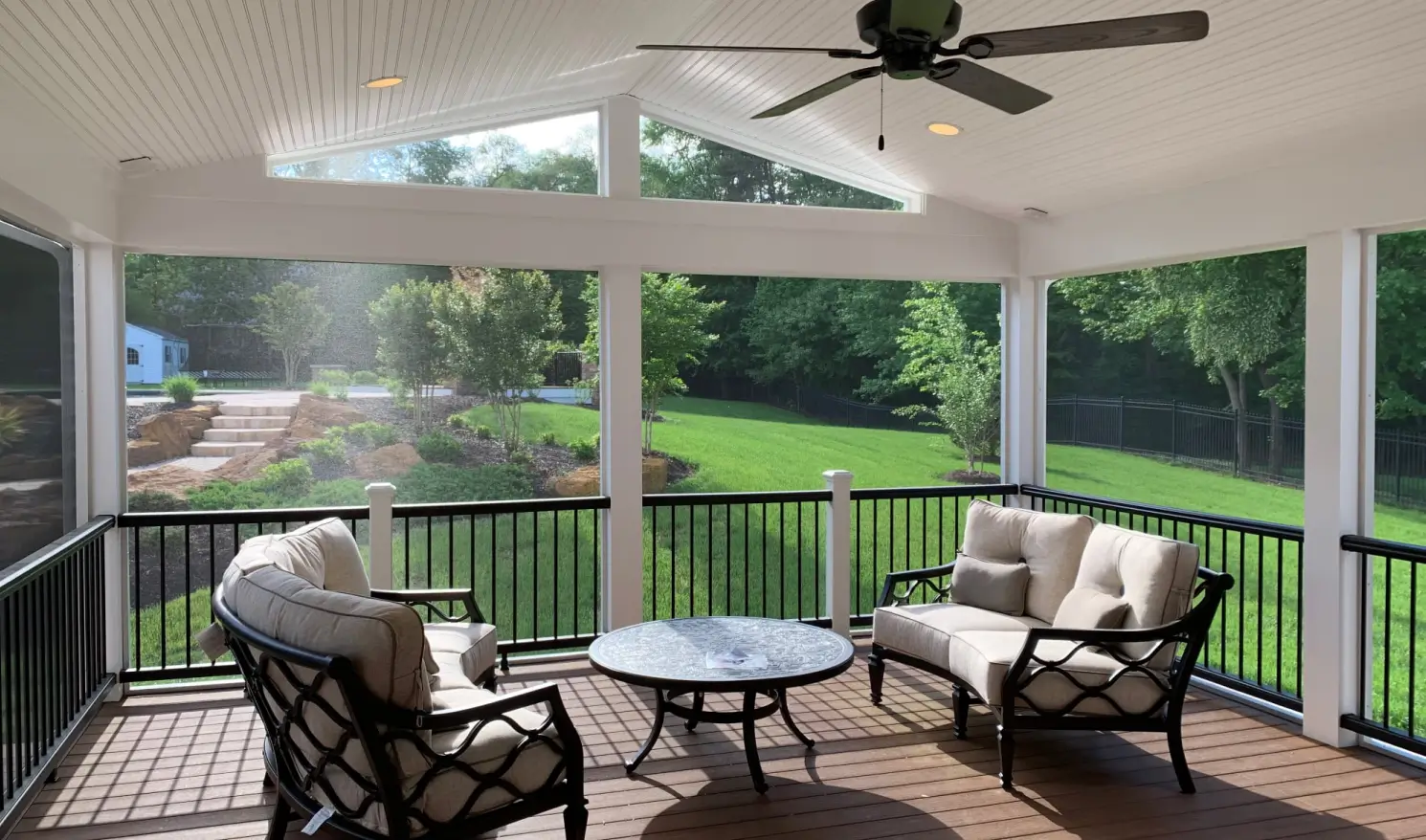 Screened patio with white ceiling, two cushioned chairs, a round table, and a view of a green backyard.