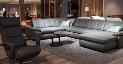 Modern living room with a large gray sectional sofa, a matching armchair, round coffee table, and soft lighting.