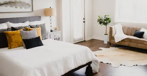 Bright bedroom with a bed, cushioned sofa, potted plant, and a cowhide rug on wooden floors.