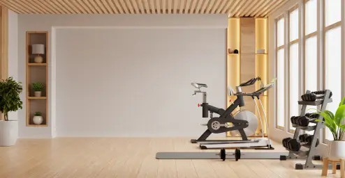 A modern home gym with exercise bike, weights, and plants by large windows and wooden shelves.