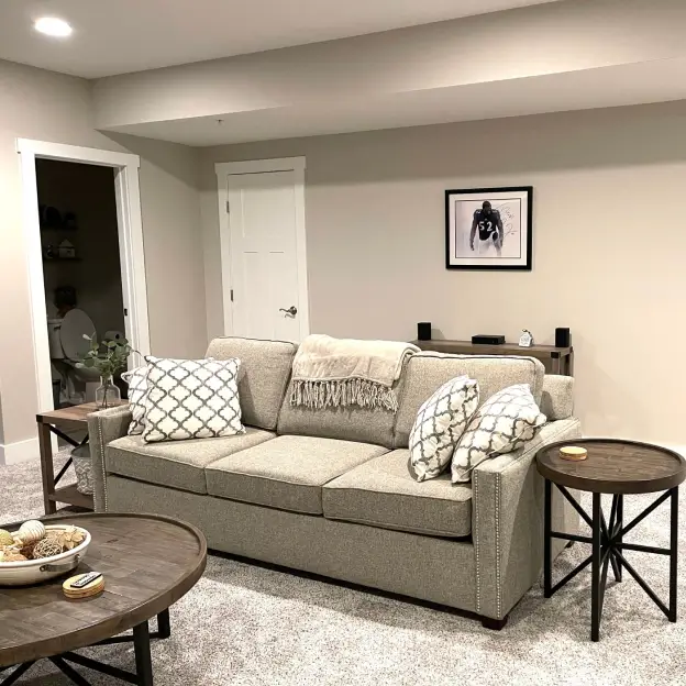 Cozy living room with a gray sofa, patterned pillows, round wooden tables, and framed wall art above.