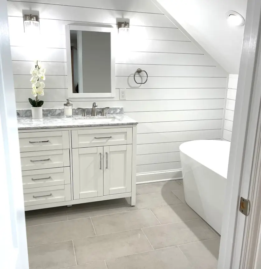 White bathroom with shiplap walls, a freestanding tub, and a vanity with double sinks and orchid decoration.