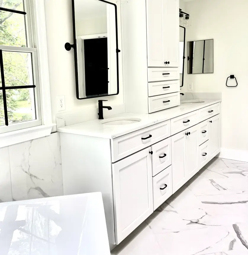 Bright bathroom with dual sinks, white cabinetry, marble tile floor, and large windows.