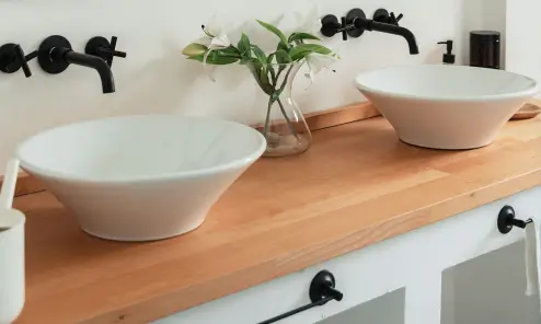 Modern bathroom with two white vessel sinks on a wooden countertop and flowers in a vase.