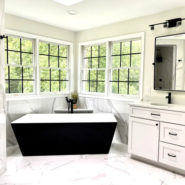 Modern bathroom with black tub, white vanity, and large windows overlooking greenery.