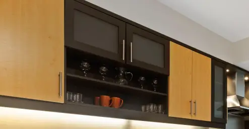 Wooden kitchen cabinets with a row of glasses and orange mugs on open shelves.