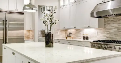Modern kitchen with white cabinets, stainless steel appliances, and a large island with a vase of flowers.