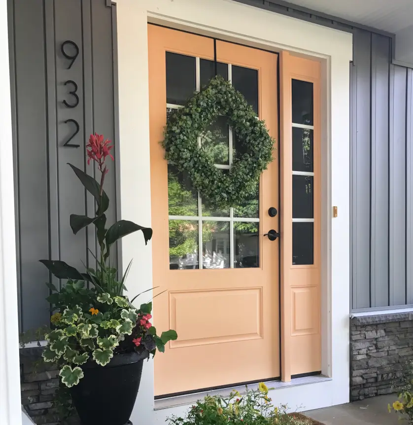 Peach-colored front door with a green wreath and potted plants beside it. House number 932 is on the wall.