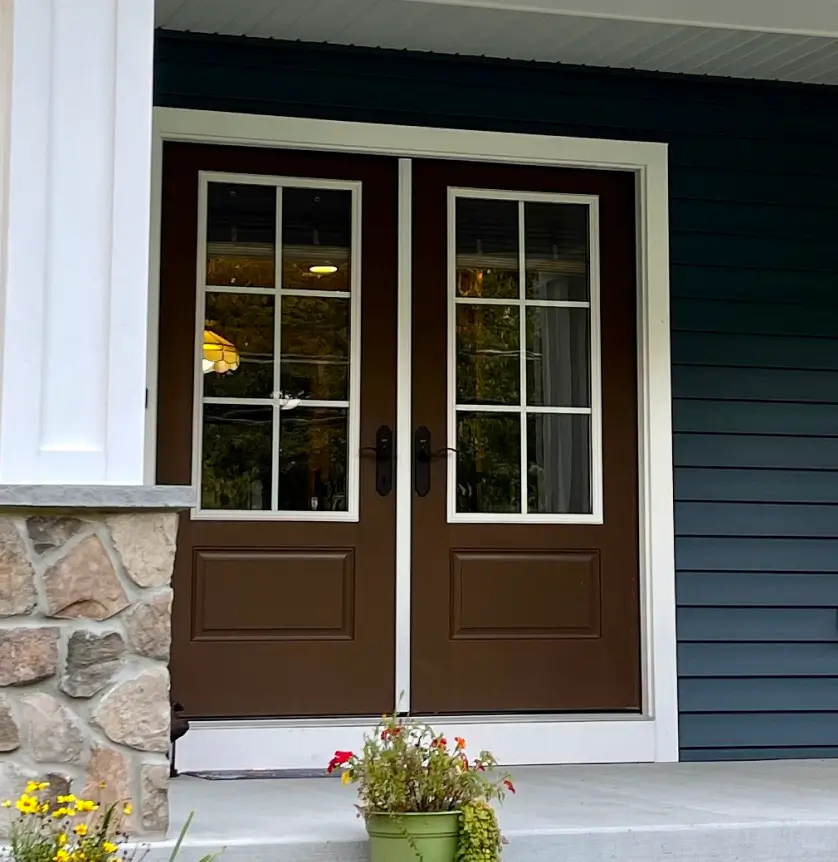 Brown double doors with glass panels, blue siding, stone wall, potted flowers on porch.