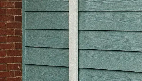Brick wall meeting with teal siding panels on a building exterior.
