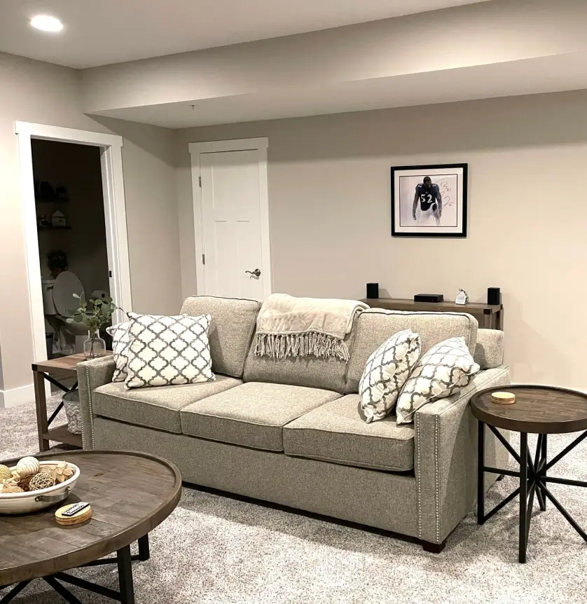 Cozy living room with a beige sofa, patterned pillows, circular wooden tables, and wall art on beige walls.