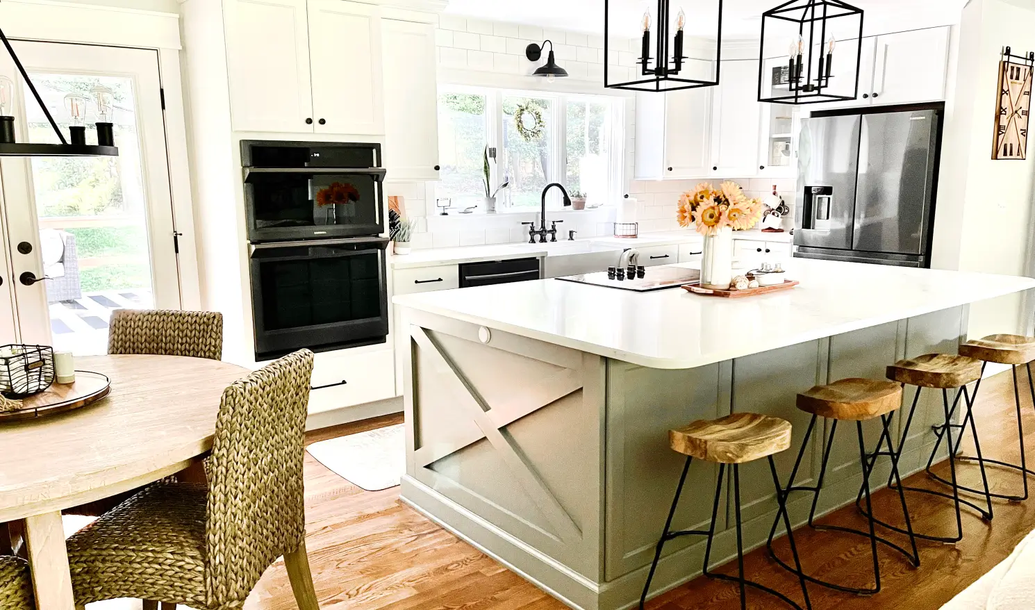 Bright kitchen with white cabinets, large island, bar stools, steel appliances, and a round dining table with chairs.