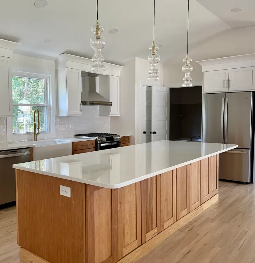 Modern kitchen with wood island, white countertops, pendant lights, stainless steel appliances, and light wood flooring.