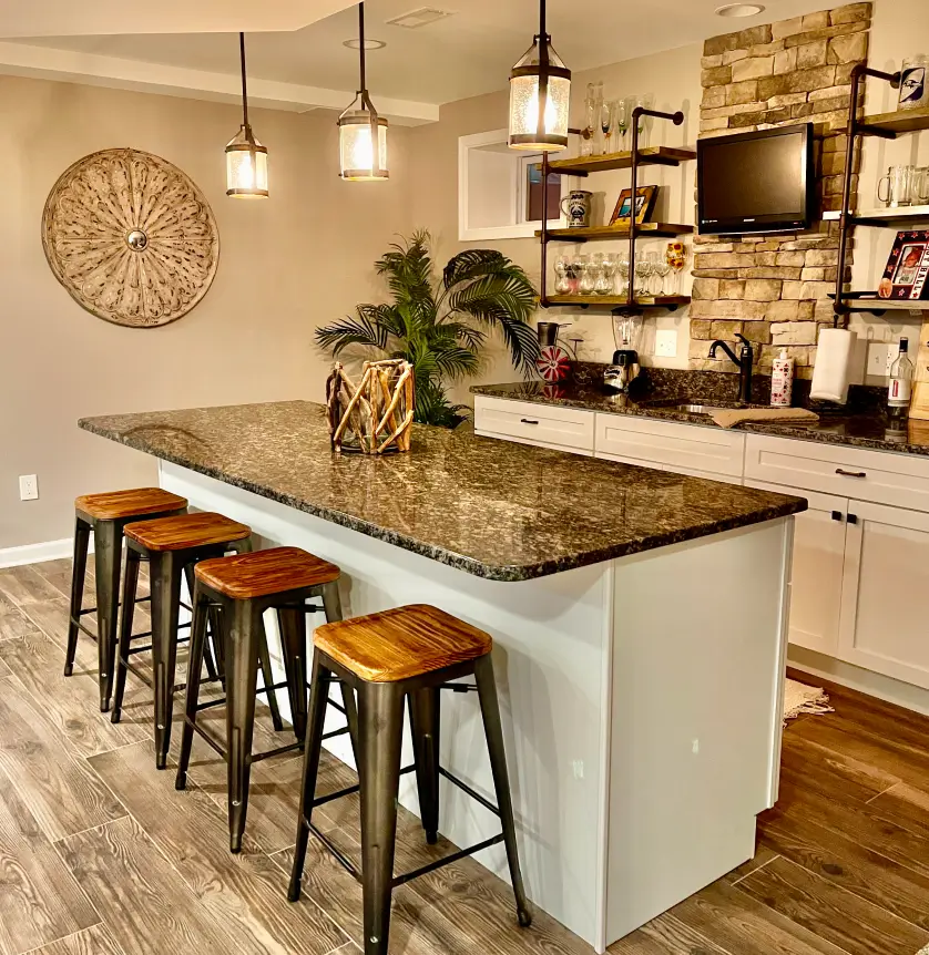 Modern kitchen with stone accent wall, island with stools, pendant lighting, and dark wood flooring.