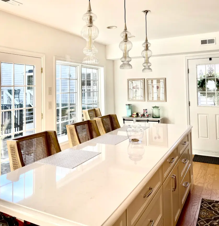 Bright kitchen with a large white island, wicker chairs, pendant lights, and glass doors leading outside.