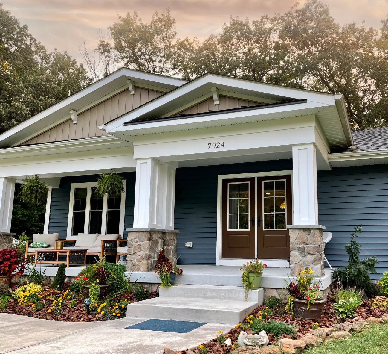 Charming blue house with a white porch, stone accents, and a garden filled with colorful flowers.