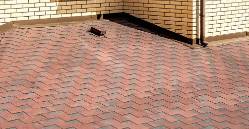 Red shingle roof with a chimney and brick walls in the background.
