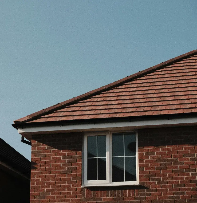 Red brick house with a tiled roof and white-framed window, set against a clear blue sky.