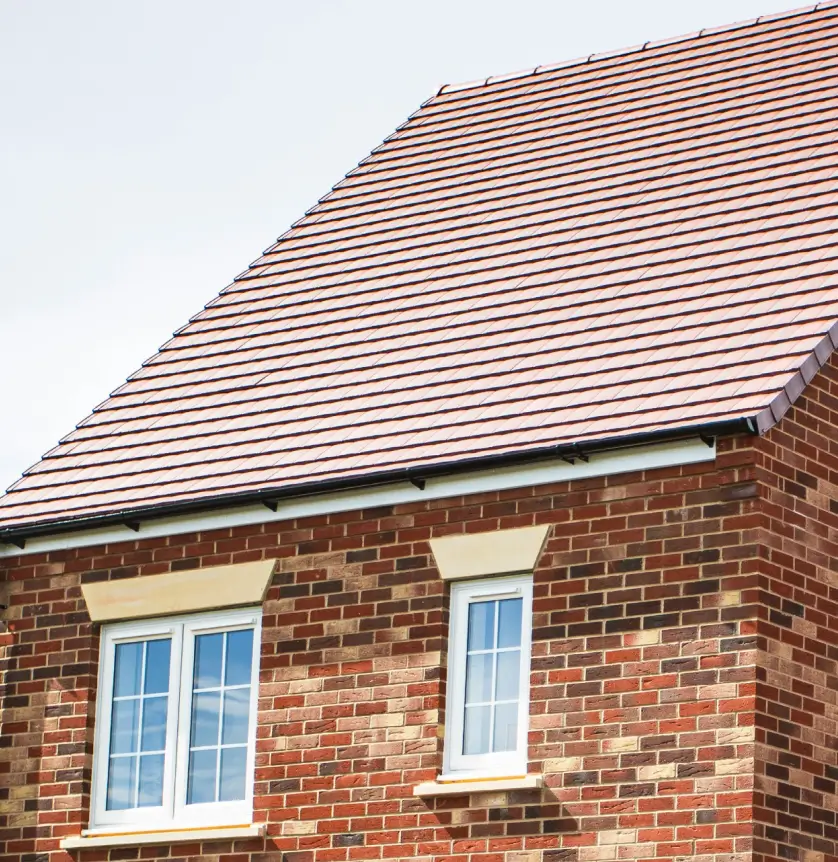 Brick house with a steeply pitched roof and two windows on the upper floor against a clear sky.