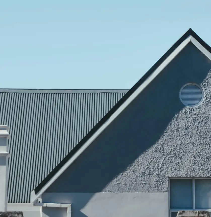 Triangular roof with a circular window and textured wall, set against a clear blue sky.