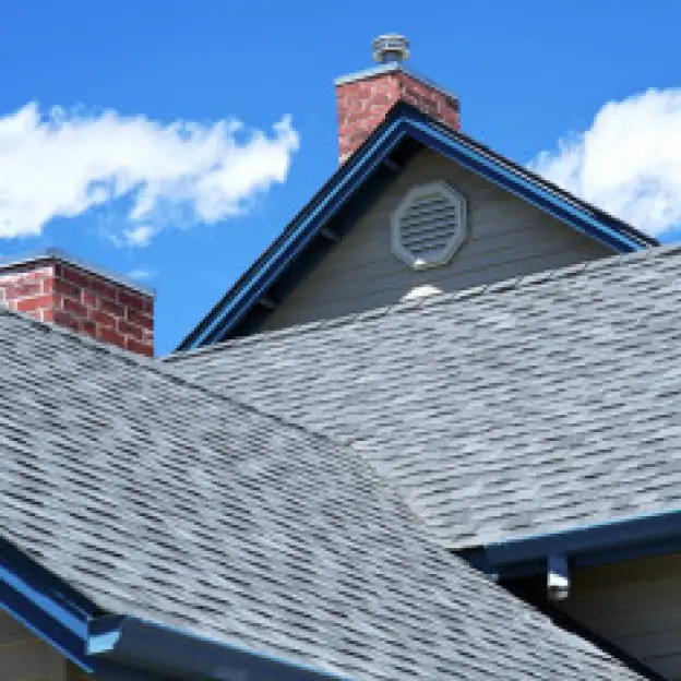Residential rooftops with gray shingles, blue trim, and brick chimneys under a clear blue sky.