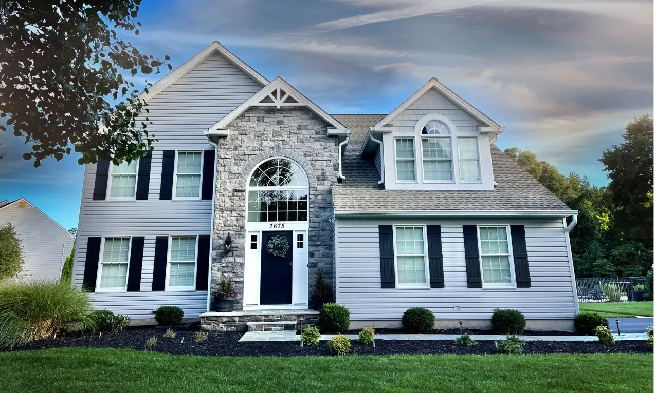 Two-story house with stone accents, arched window above front door, and neatly trimmed lawn under a blue sky.