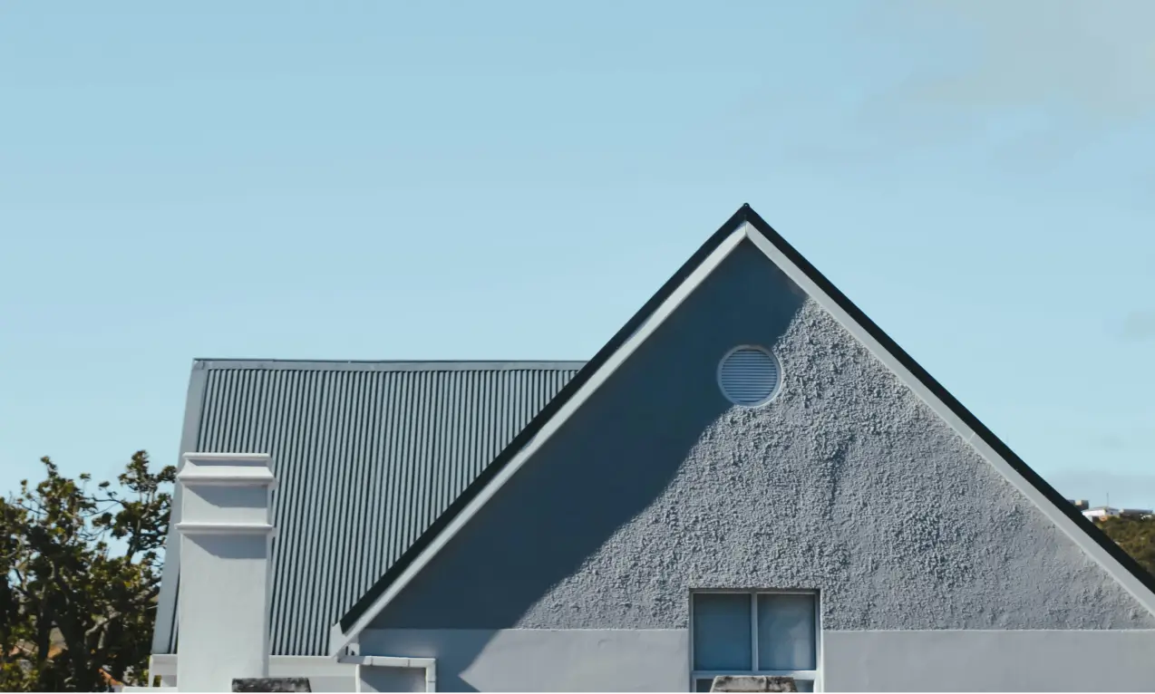 A blue house with a triangular roof and a circular window against a clear sky.