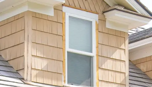 A beige house exterior with a double-hung window and shingled walls under a sloped roof.