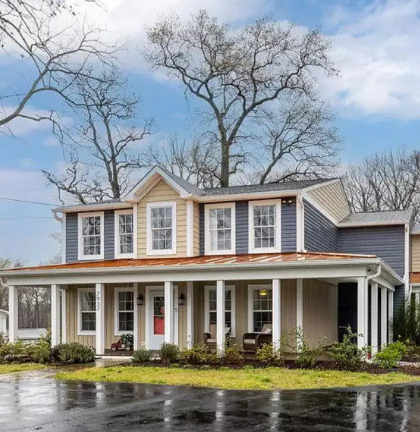 Two-story house with a porch, surrounded by trees, on a rainy day.
