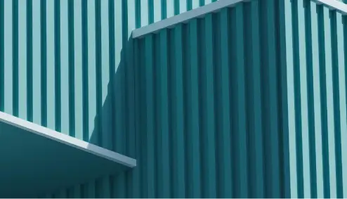 Close-up of a teal corrugated metal wall with diagonal shadows creating a geometric pattern.