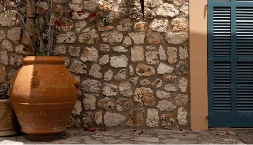 Large terracotta pot beside a stone wall with green shuttered window.