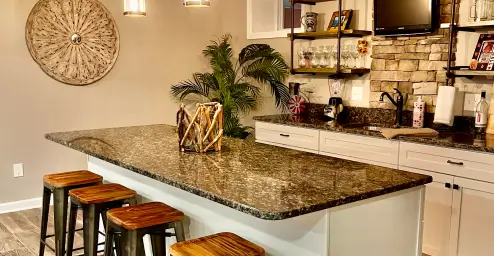 Modern kitchen with a granite island, wooden stools, decorative wall piece, and open shelving.