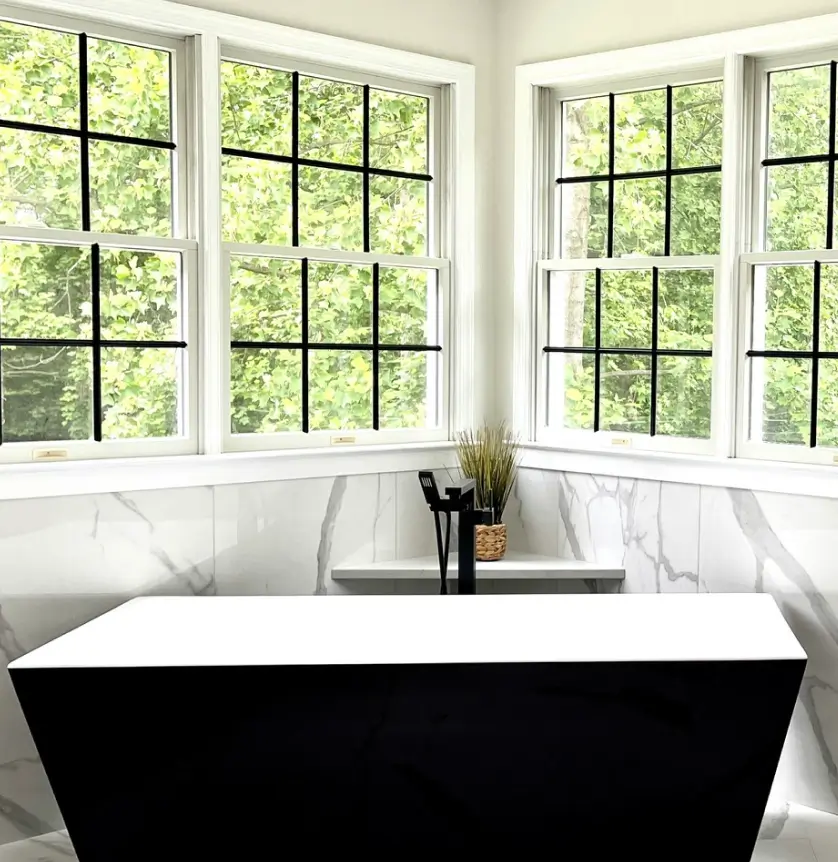 Contemporary bathroom with a freestanding tub and large windows overlooking lush green trees.