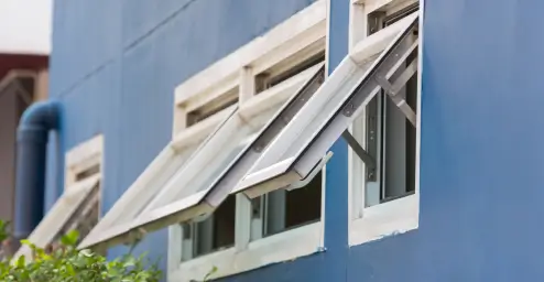 Tilted windows on a blue building wall with open panes, and nearby greenery.