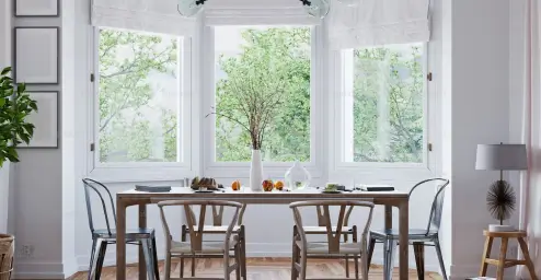 Bright dining room with a table, chairs, and large windows overlooking lush green trees.