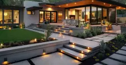 Modern house with large glass doors, lit garden steps, and a neatly landscaped yard at twilight.