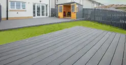 Backyard with grey decking, a small grass area, a wooden shed, and a modern house in the background.