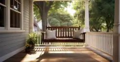 Wooden porch swing with cushions, overlooking a lush green garden in bright sunlight.