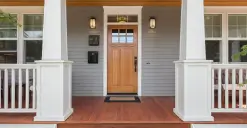 A wooden front door with a porch, white railings, and two wall lanterns.