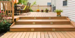 Wooden deck with three steps, potted plants, and a patio table set under a sunny sky.